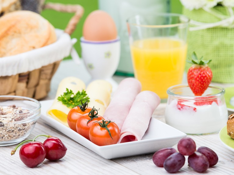 Reichgedeckter Frühstückstisch mit Schinken, Tomaten, Saft