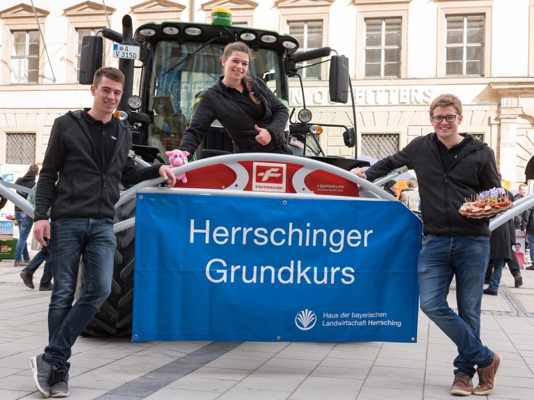 Mit einem Traktor stehen drei junge Landwirte des Herrschinger Grundkurses in der Innenstadt von München