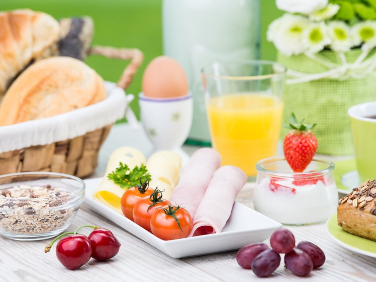 Ein Tisch der reichlich mit ausgewogenen Lebensmitteln wie Orangensaft, Eier, Brotkörbchen, Tomaten und Aufstrich gedeckt ist.