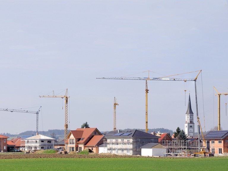 Auf den Feldern rund um ein Dorf werden neue Häuser gebaut und Flächen so verbraucht