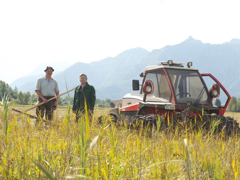 Zwei Landwirte unterhalten sich auf einen Feld. Im Hintergrund ein Schlepper zu sehen