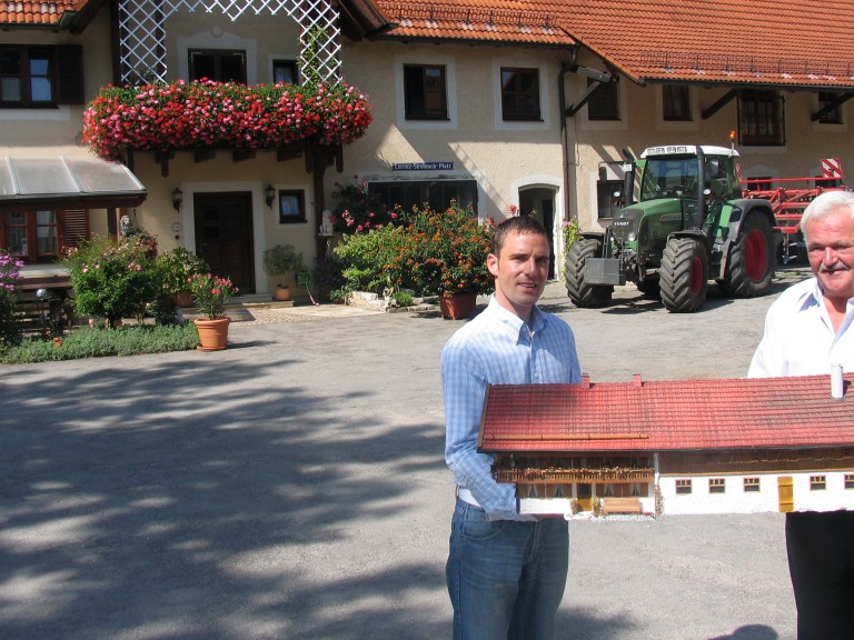 Ein junger und ein alter Landwirt stehen vor ihrem Hof 
