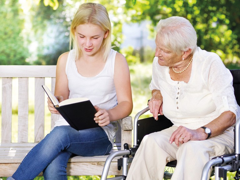 Frühzeitig an das Alter denken - eine junge Frau liest einer Seniorin etwas vor.