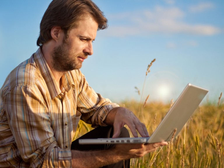 Mann sitzt mit Laptop im Feld