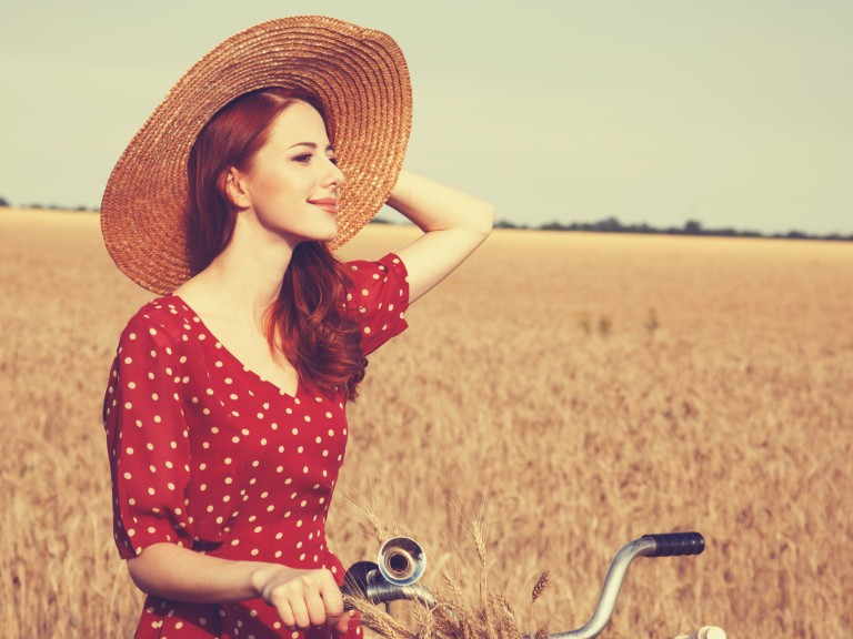 Junge Landfrauen vernetzen sich auf dem Land und fahren in roten Kleidern Fahrrad über Felder