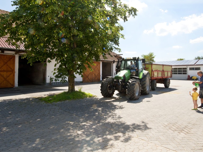 Eine Hofstelle mit Traktor und Menschen in der Mitte