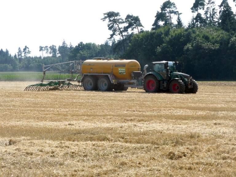 Ein Schlepper bringt mit seinem Güllefass Gülle auf Stroh aus.