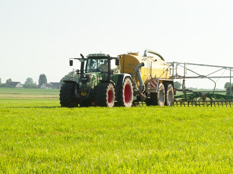 Ein Landwirt bringt mit seinem Traktor und Fass Gülle auf einer Wiese aus.