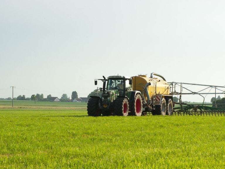 Ein Landwirt mit Traktor und Güllefass bei der Düngung einer Wiese. 