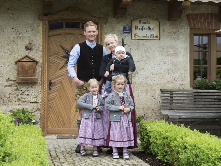 Eine junge Bauernfamilie steht vor Ihrem Hauseingang. 