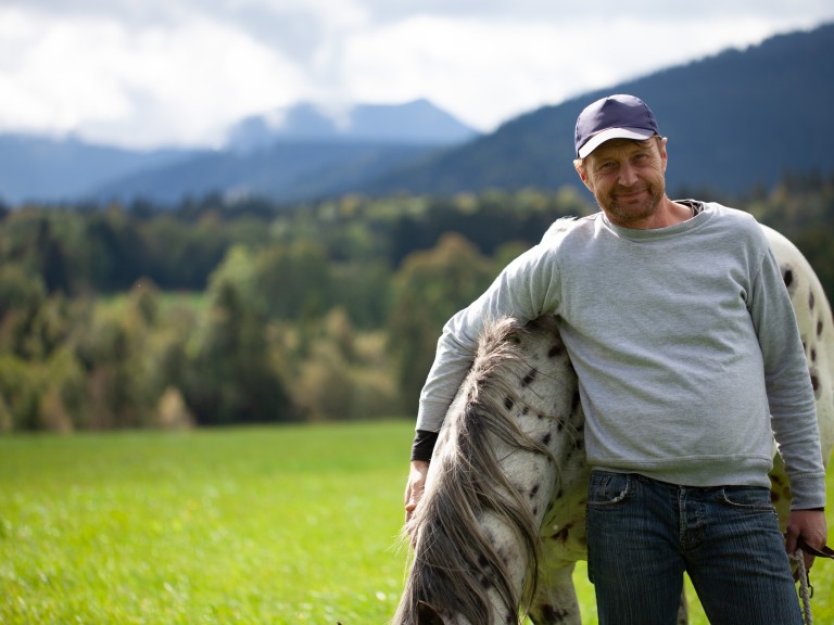 Mann steht neben Pferd auf Wiese und legt Arm um Pferd