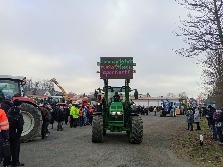 Fahrender Schlepper mit Prottesttafel an erhobener Frontgabel