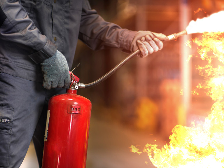 Mensch richtet Feuerwehrlöscher auf Flammen