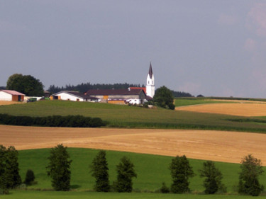 Im Vordergrund ist ein Getreidefeld, im Hintergrund ein Dorf zu sehen.