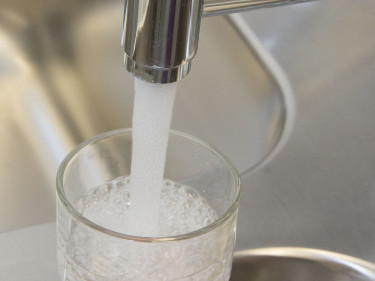 Aus dem Wasserhahn wird Wasser in ein Glas gefüllt