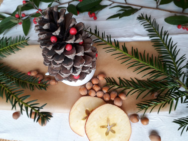 Eine festliche Tischdekoration mit Materialien aus der Natur wie Tannenzapfen, Äpfeln und Tannenzweigen. 