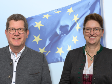 Herr Köhler und Frau Singer stehen vor der EU Flagge