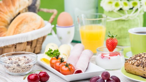 Ein Tisch der reichlich mit ausgewogenen Lebensmitteln wie Orangensaft, Eier, Brotkörbchen, Tomaten und Aufstrich gedeckt ist. 
