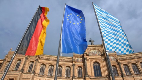 Die Deutschland-, Eu-, und Bayernfahne vor einem historischen Gebäude
