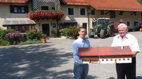 Ein junger und ein alter Landwirt stehen vor ihrem Hof 