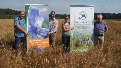 Beim Pressetermin Ackerwildkrautschutz stehen die Organisator mit den Rollups in einem Feld