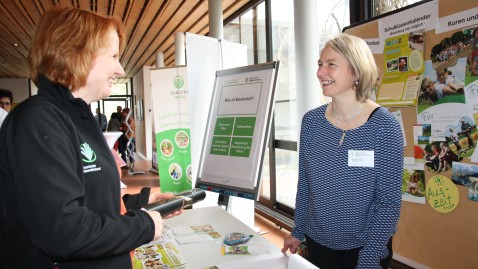 Landfrauen im Dialog am Tisch bei einer Ausstellung. 