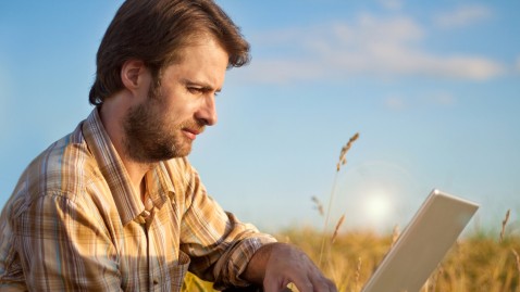 Mann sitzt mit Laptop im Feld