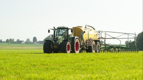 Ein Landwirt bringt mit seinem Traktor und Fass Gülle auf einer Wiese aus.