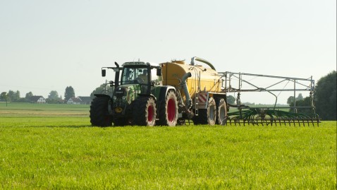 Ein Landwirt mit Traktor und Güllefass bei der Düngung einer Wiese. 