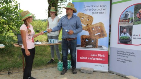 Alexander Apfelböck nutzt den SVLFG-Infostand, um eine seiner Saison-Arbeitskräfte mit einer Tube Sonnencremes auszustatten. 