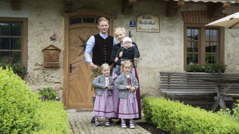 Eine junge Bauernfamilie steht vor Ihrem Hauseingang. 