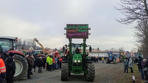 Fahrender Schlepper mit Prottesttafel an erhobener Frontgabel