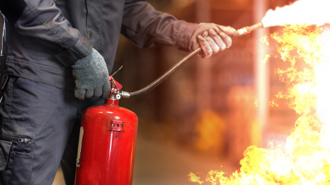 Mensch richtet Feuerwehrlöscher auf Flammen