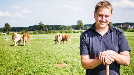 Landwirt Michael Kneißl auf seiner Weide mit grasenden Kühen im Hintergrund