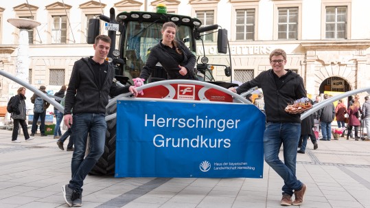 Mit einem Traktor stehen drei junge Landwirte des Herrschinger Grundkurses in der Innenstadt von München