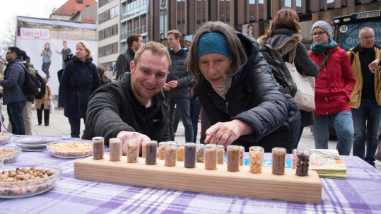 Ein junger Landwirt des Herrschinger Grundkurses zeigt einer Dame in München verschiedene Getreidesorten