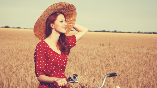 Junge Landfrauen vernetzen sich auf dem Land und fahren in roten Kleidern Fahrrad über Felder