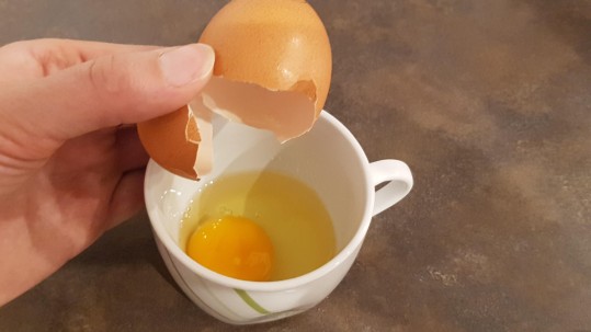 Ein Ei in die Tasse aufschlagen.