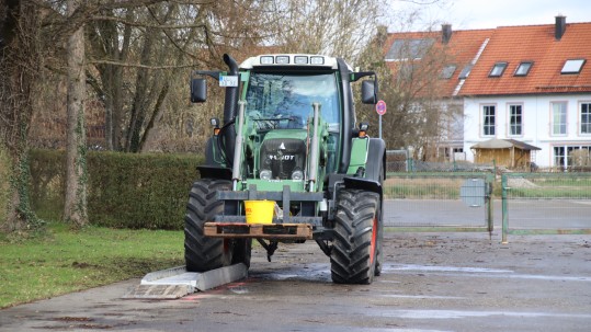 Schlepper balanciert Wassereimer über Hindernusparcours.